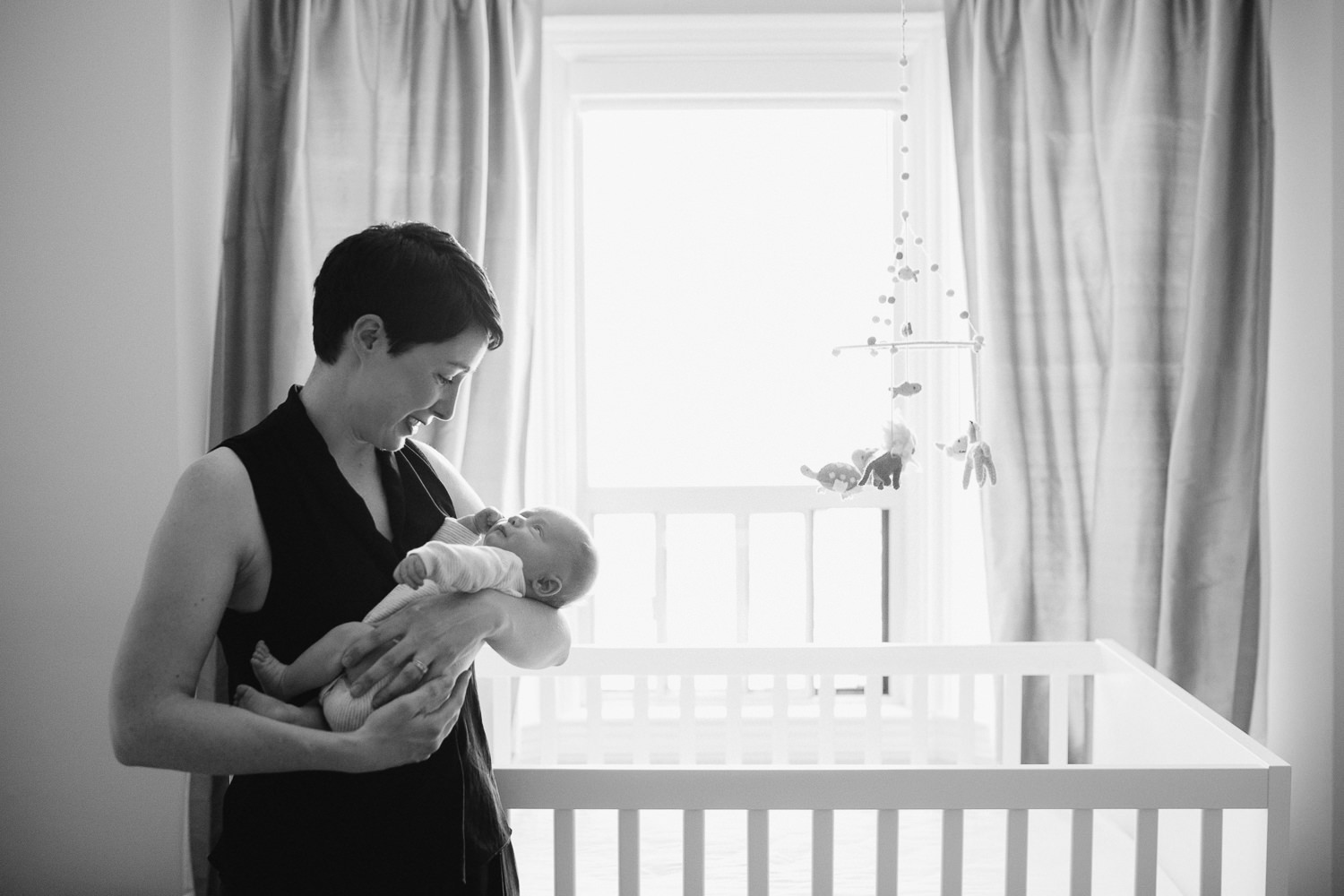 first time mom holding baby boy standing in front of nursery crib - Markham In-Home Photos