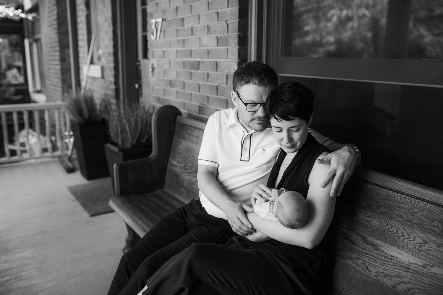 new parents sitting on front porch holding sleeping 2 week old baby boy - Markham In-Home Photos