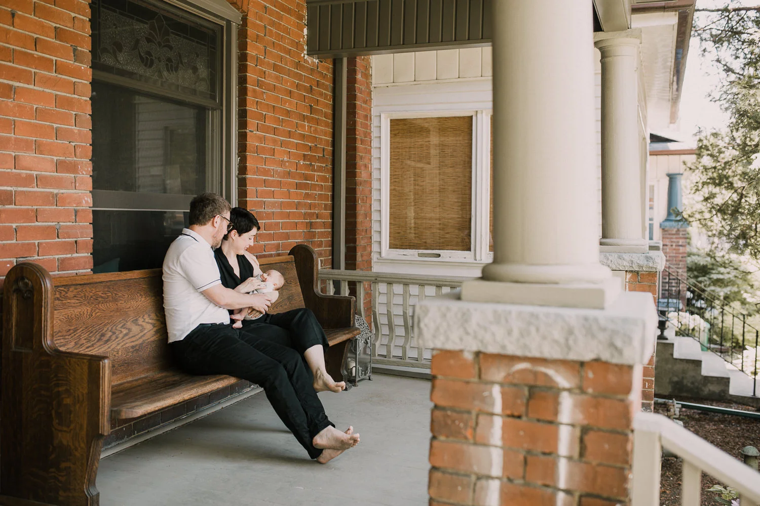 new parents sitting on front porch holding sleeping 2 week old baby boy - Stouffville In-Home Photos