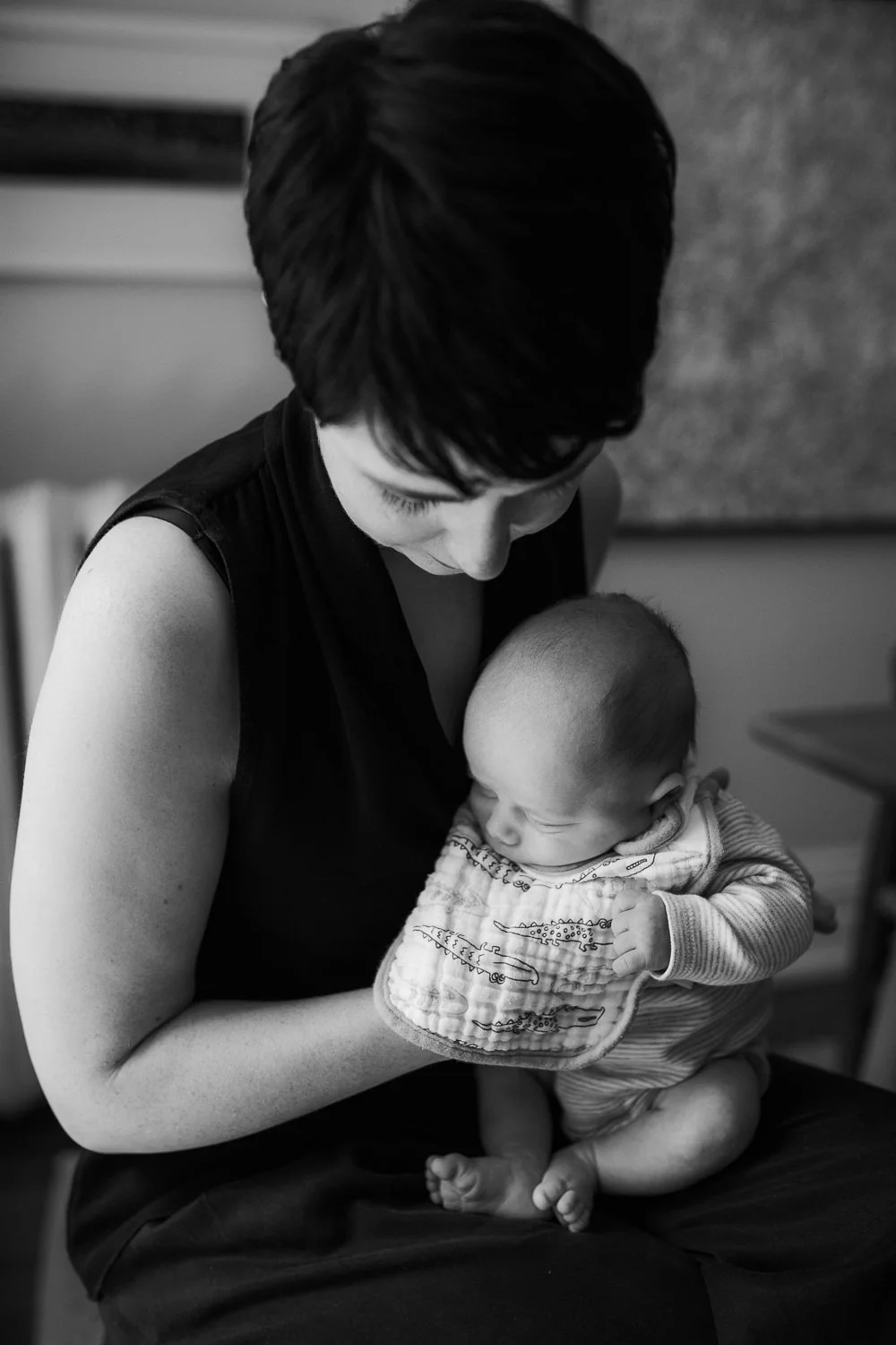first time mom sitting in dining room chair burping 2 week old baby boy with bib on - Barrie Lifestyle Photos