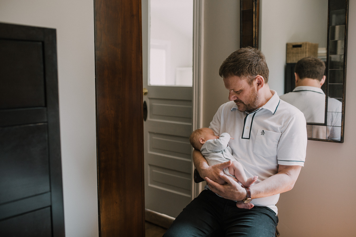 first time father sitting in chair holding and looking at 2 week old baby boy - Stouffville In-Home Photos