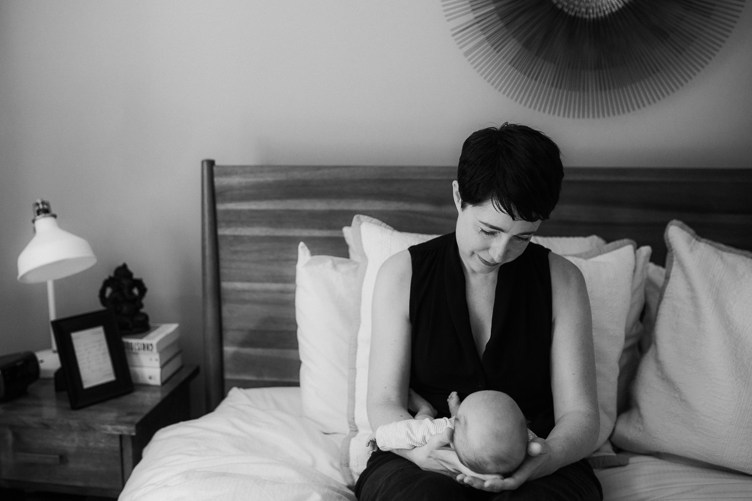 new mom sitting on master bed, 2 week old baby boy sleeping in her arms - Newmarket Lifestyle Photos