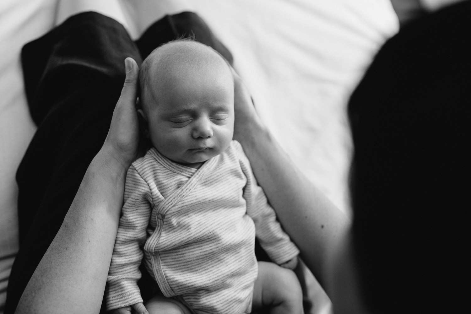 first time mother sitting on master bed, 2 week old baby boy sleeping in her lap - Stouffville Lifestyle Photos