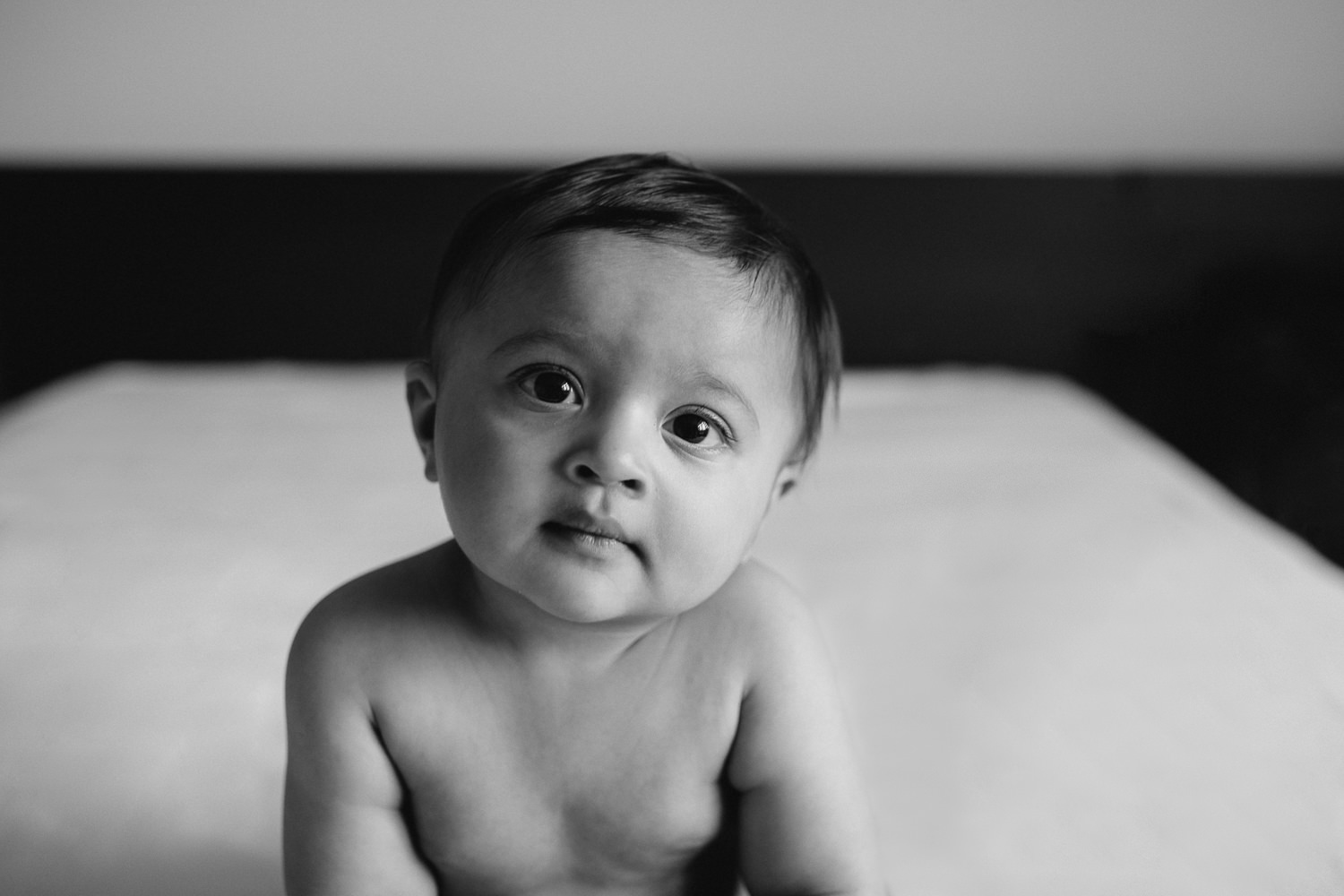 8 month old baby boy in diaper sitting on bed looking at camera - Newmarket Lifestyle Photography