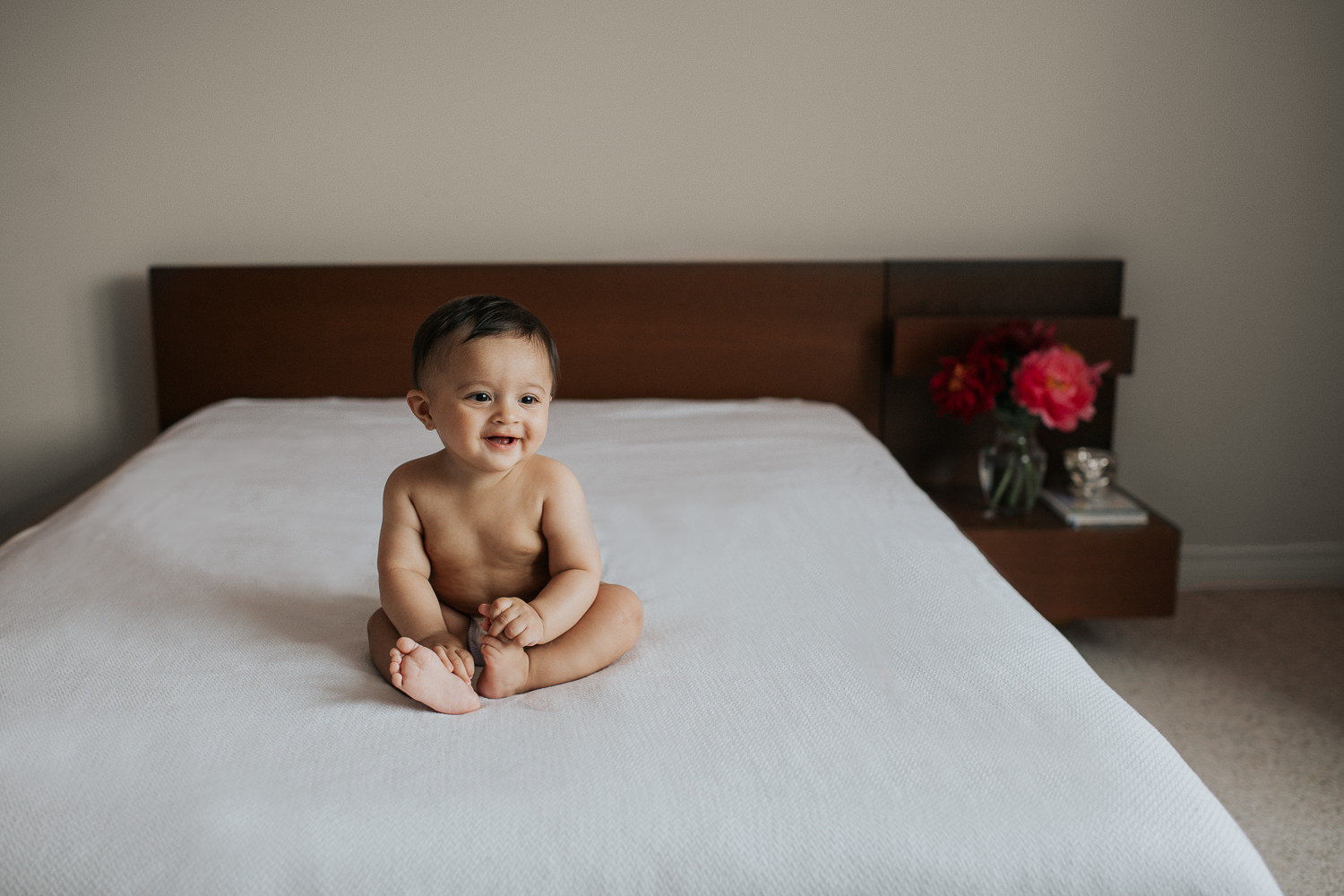 8 month old baby boy in diaper sitting on bed laughing and smiling - Stouffville Lifestyle Photography