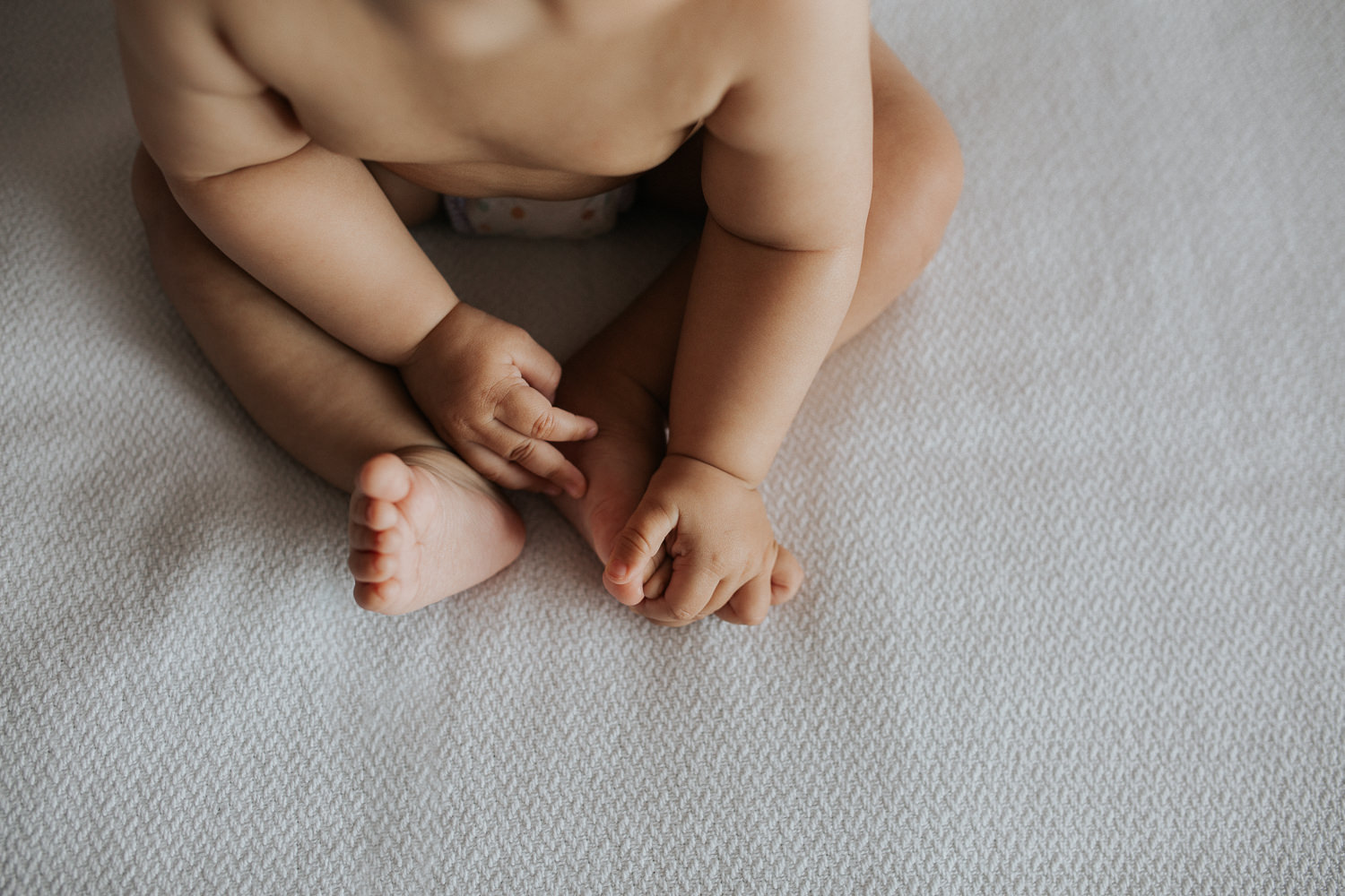 8 month old baby boy in diaper sitting on bed, close up of hands and feet - Barrie Lifestyle Photography