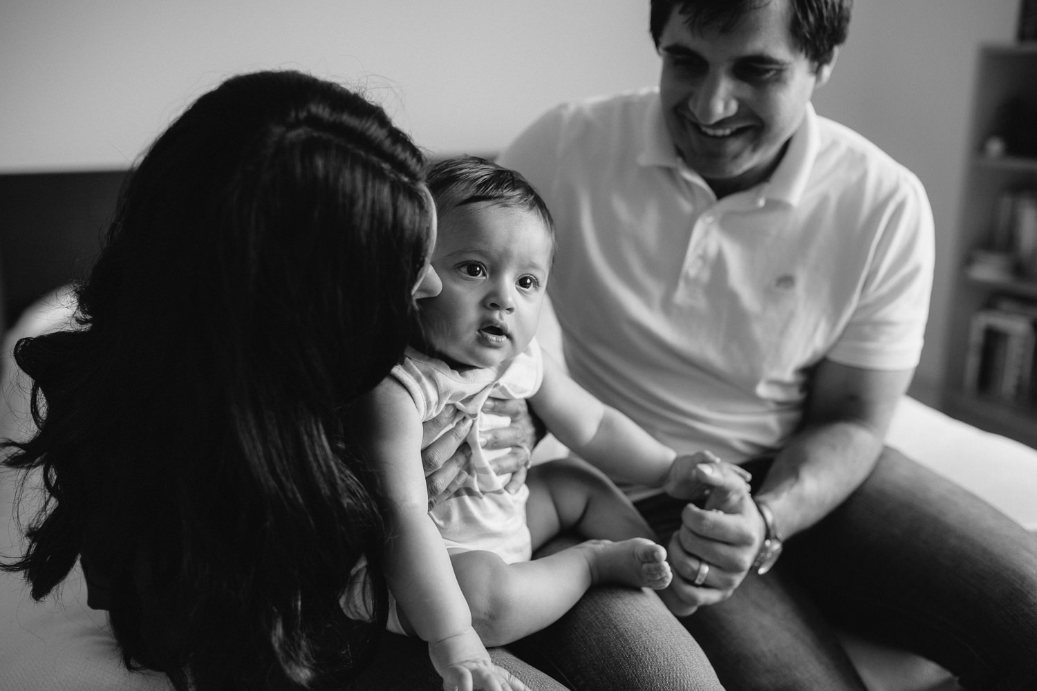 Markham Lifestyle Photosfamily of 3 sitting on bed, mom holding 8 month old baby boy in lap, kissing his cheek -