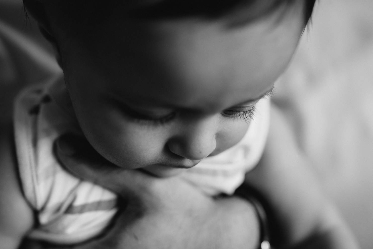 8 month old boy sitting in dad's lap, close up of eyelashes as he looks down - Markham In-Home Photos