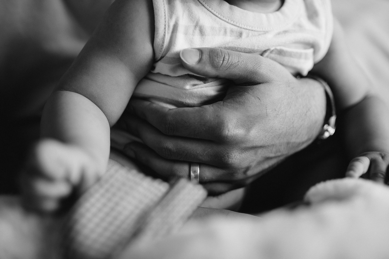 8 month old baby boy sitting in dad's lap, close up of father's hand around son's middle - Barrie In-Home Photos