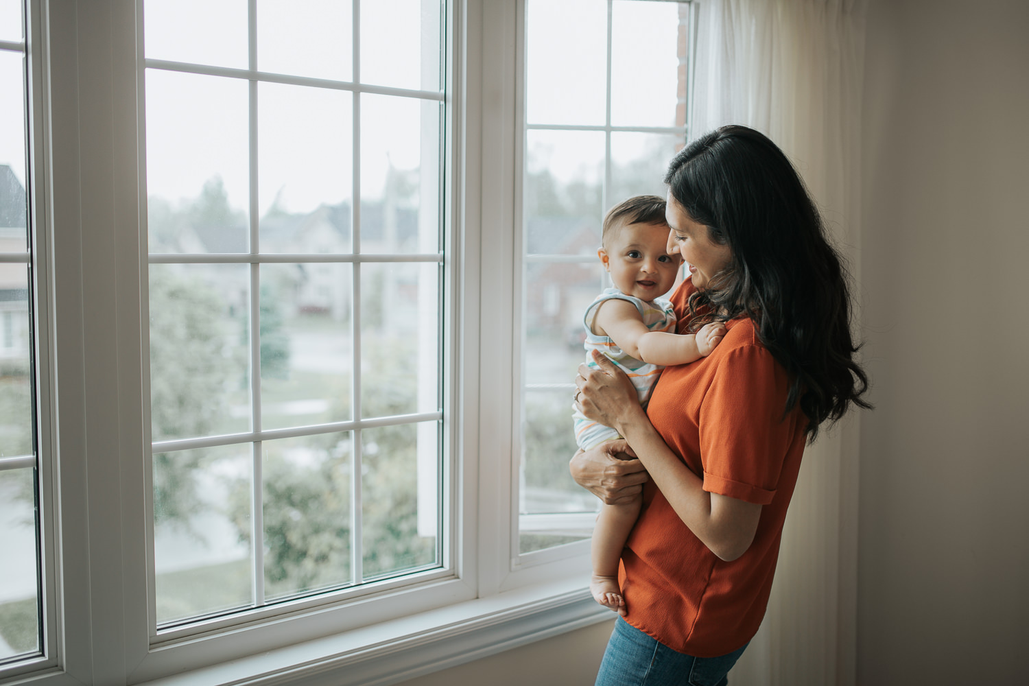 mom standing at window with 8 month old baby boy who is smiling at camera -  Newmarket Lifestyle Photos