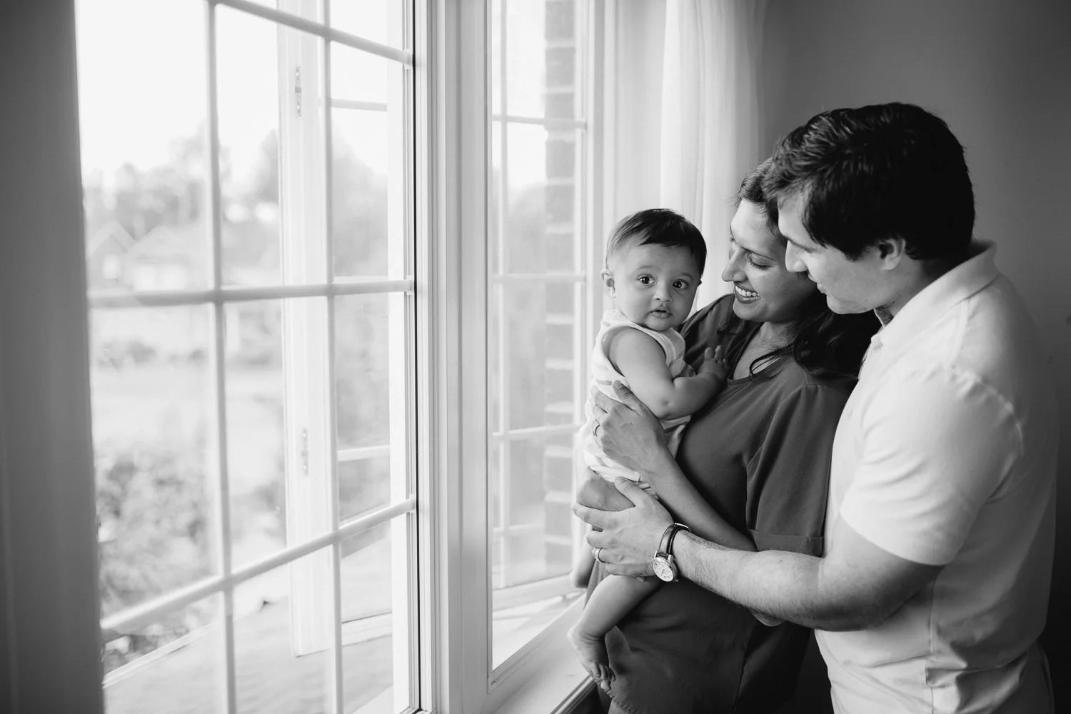 family of 3 standing at window, mom holding 8 month old baby boy - Barrie Lifestyle Photos