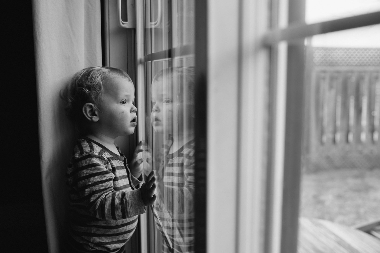 blonde 18 month old boy standing at window looking outside, can see reflection - Markham Family Photographs