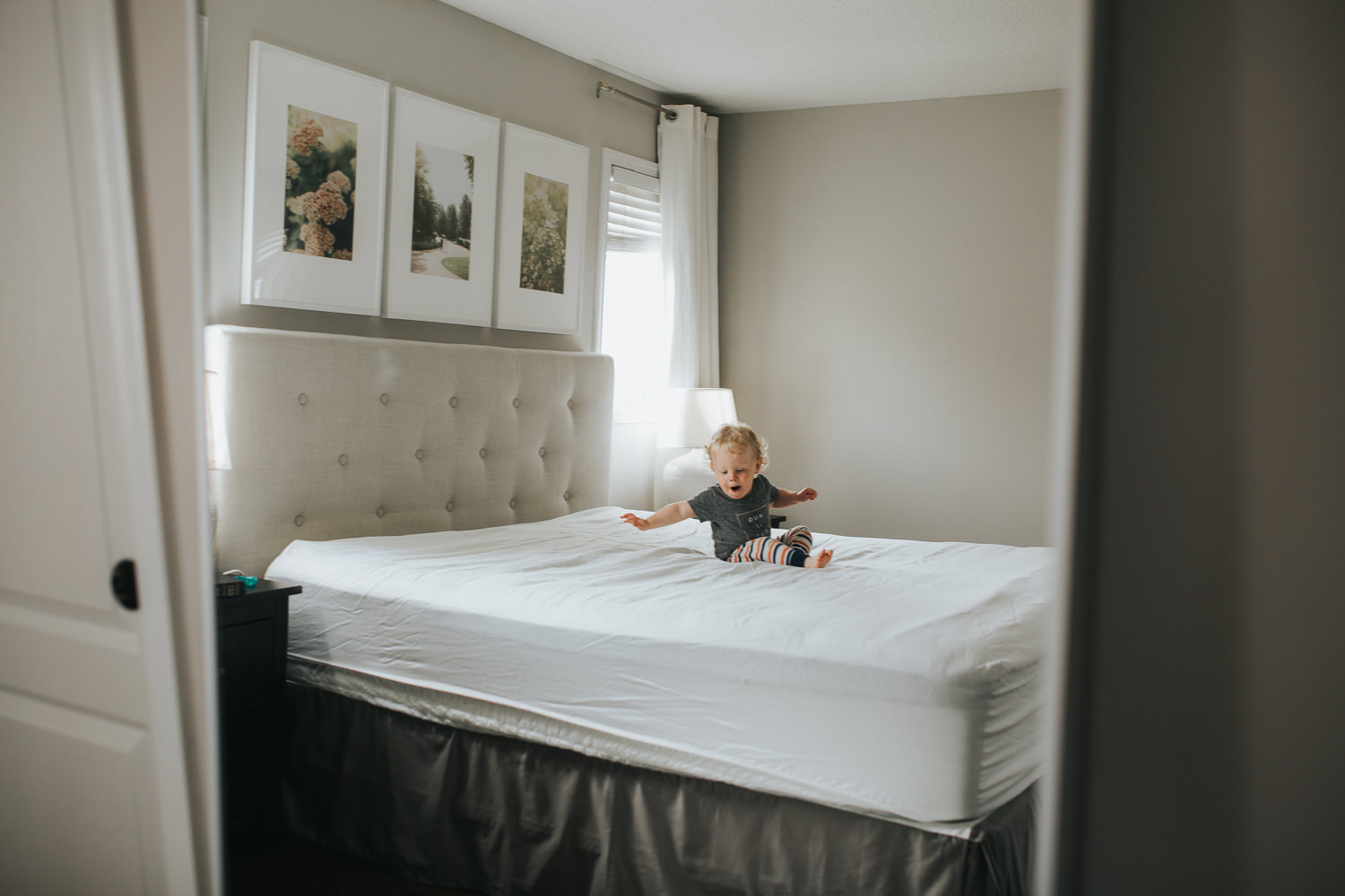 18 month old boy with blonde hair jumping on parent's bed - Stouffville Documentary Photographs