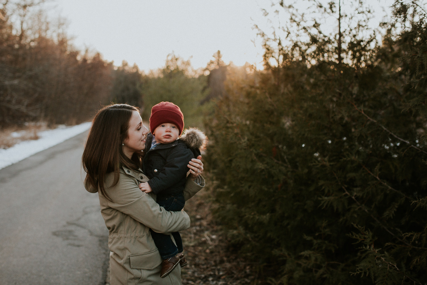 mom holding 18 month old boy in red hat in the woods at sunset - Stouffville Family Photographs