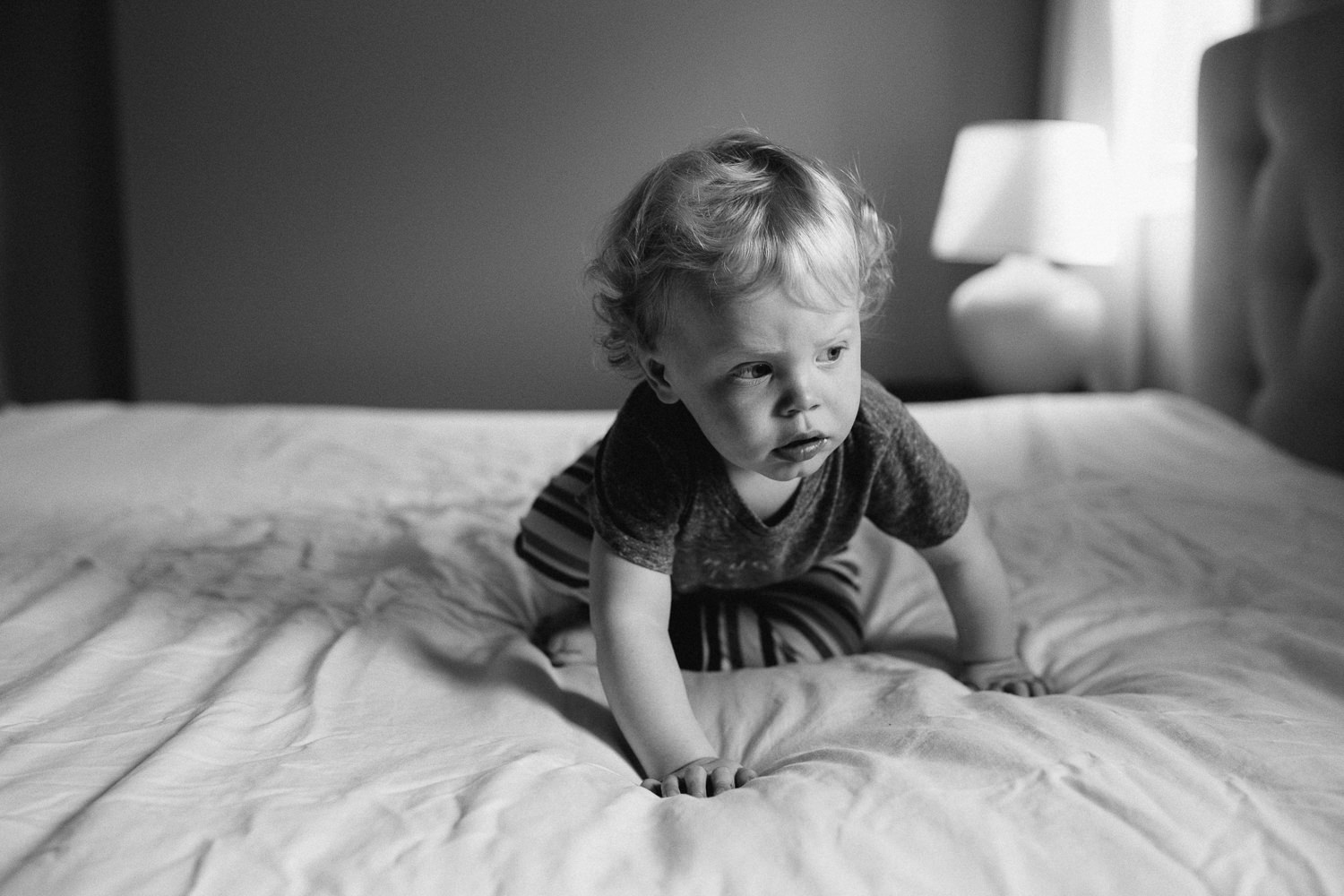 toddle boy with curly hair crawling on bed, looking to the side - Barrie Documentary Photographs