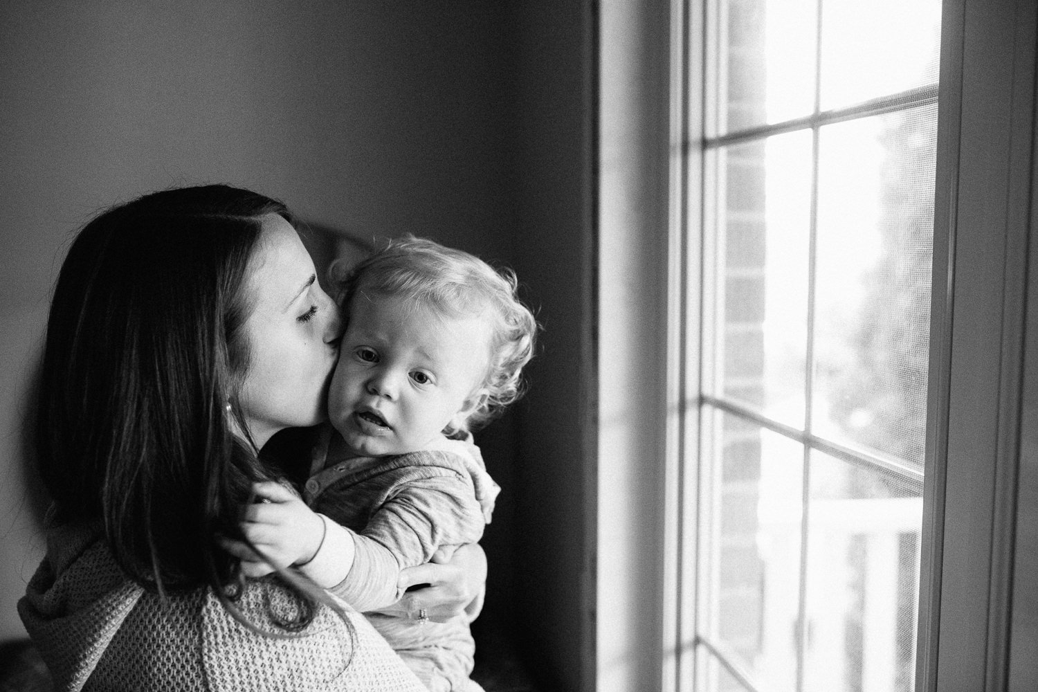 mom kissing 18 month old son on cheek, standing by window - Newmarket Family Photography