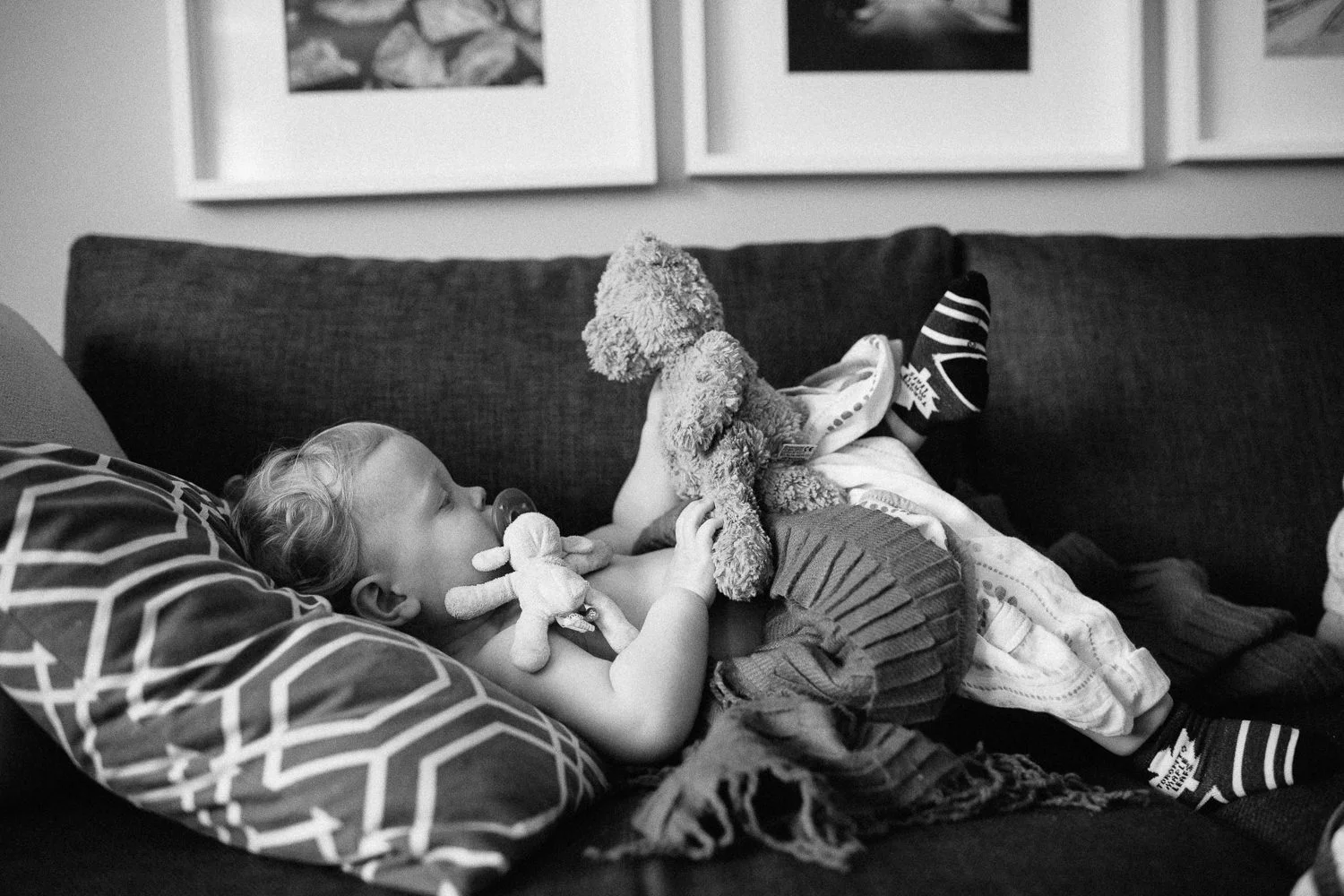 toddler lying on couch with soother in his mouth, holding and looking at teddy bear - Newmarket Family Photography