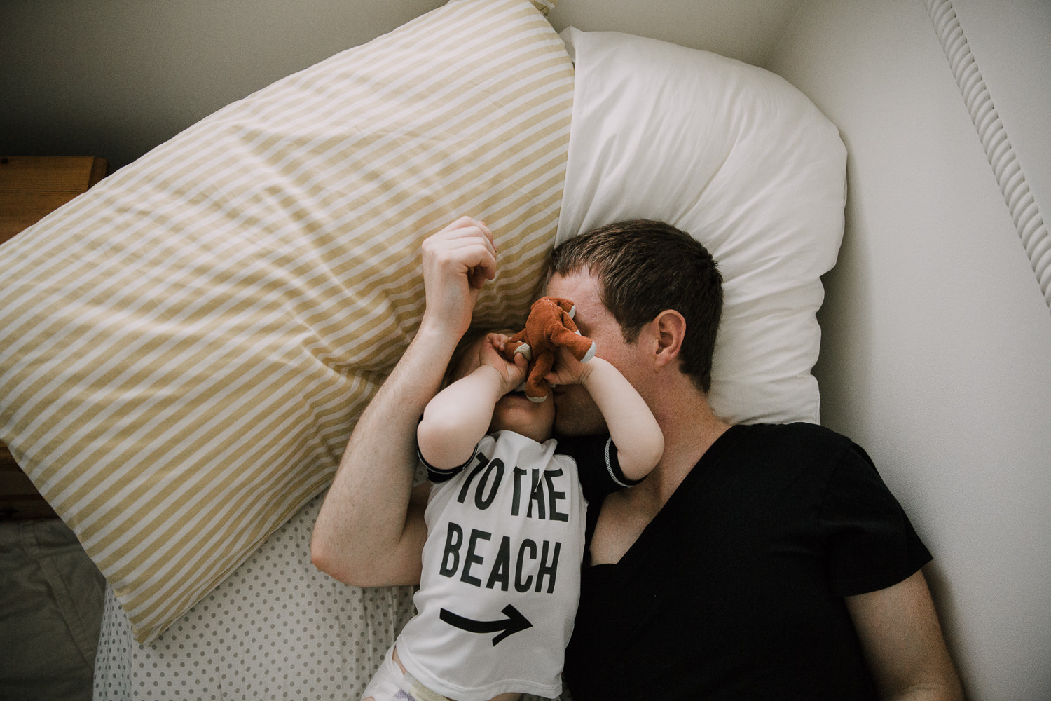 Father and toddler son lying on bed, dad kissing boy on cheek - Newmarket Family Photographer