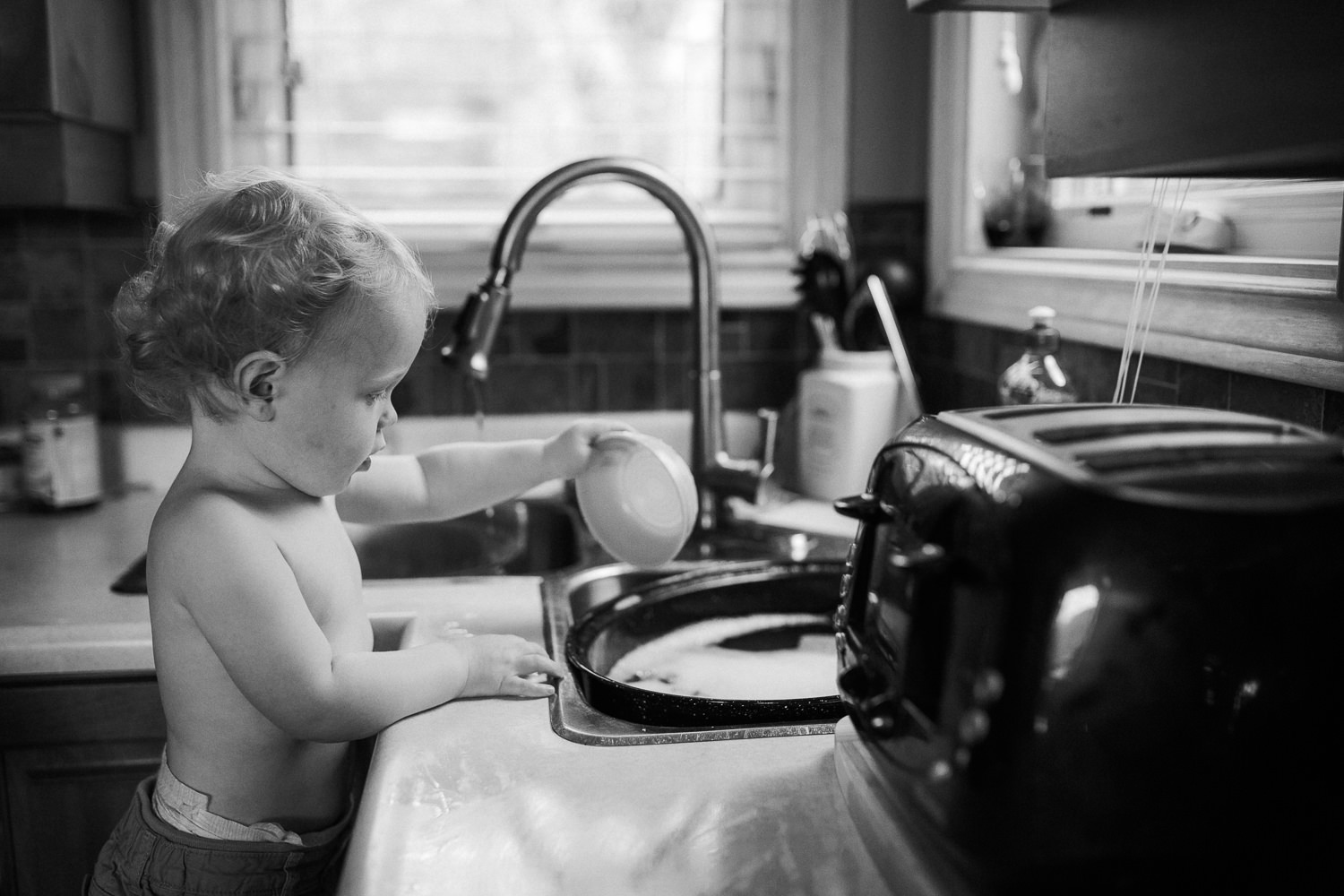 blonde toddler boy playing at kitchen sink with bowl and water - Newmarket Family Memories