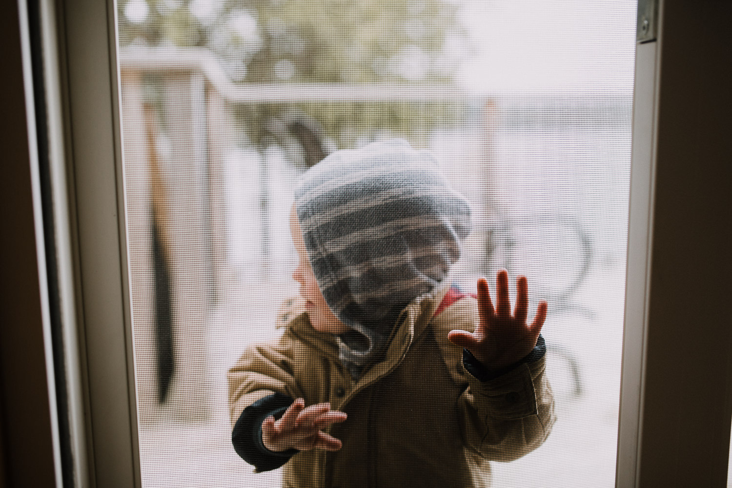 toddler boy in coat and hood outside, pressing hands against screen door - Markham Documentary Photographer