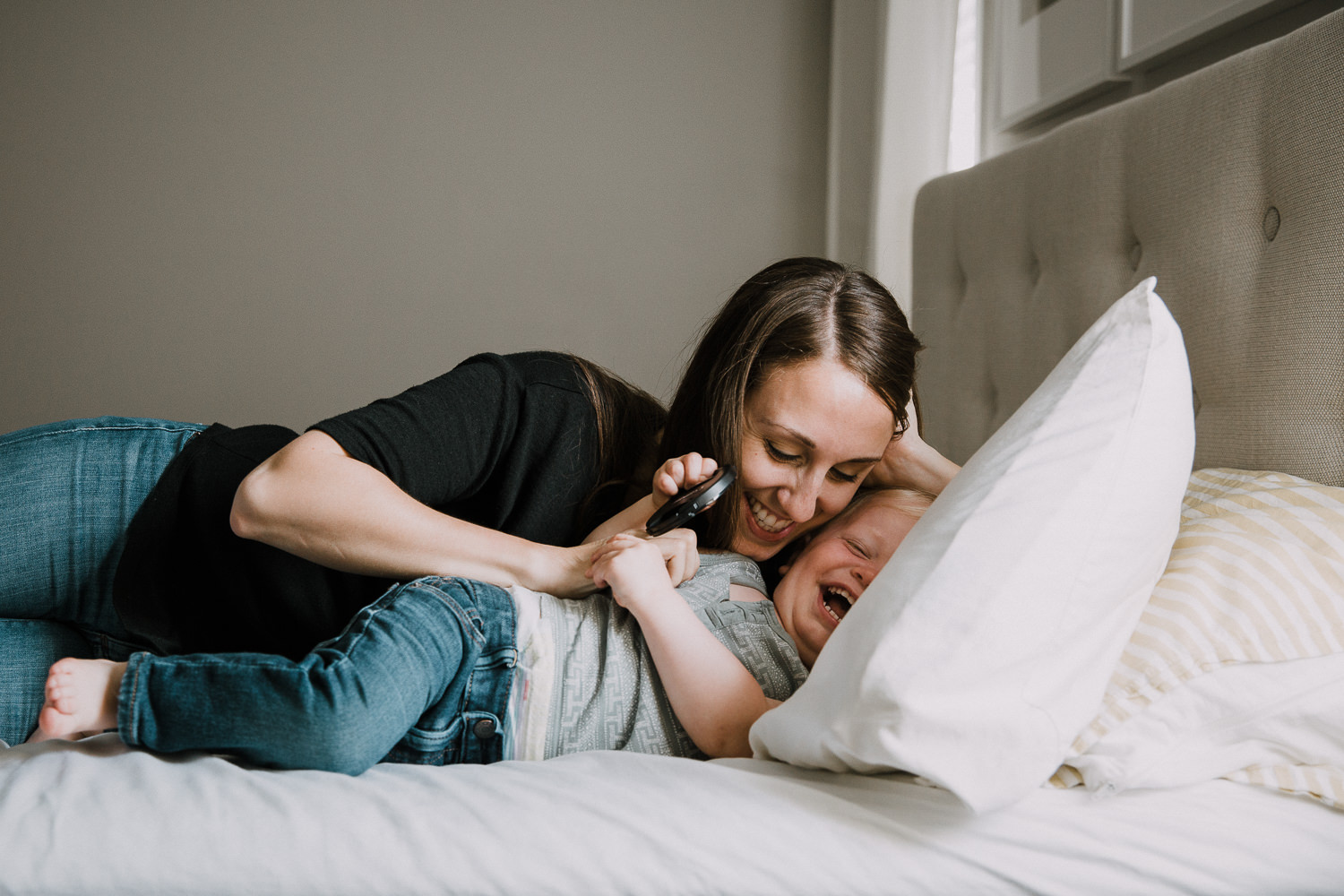 mom and toddler boy lying on bed, mother tickling boy as he laughs - Barrie Family Photographer