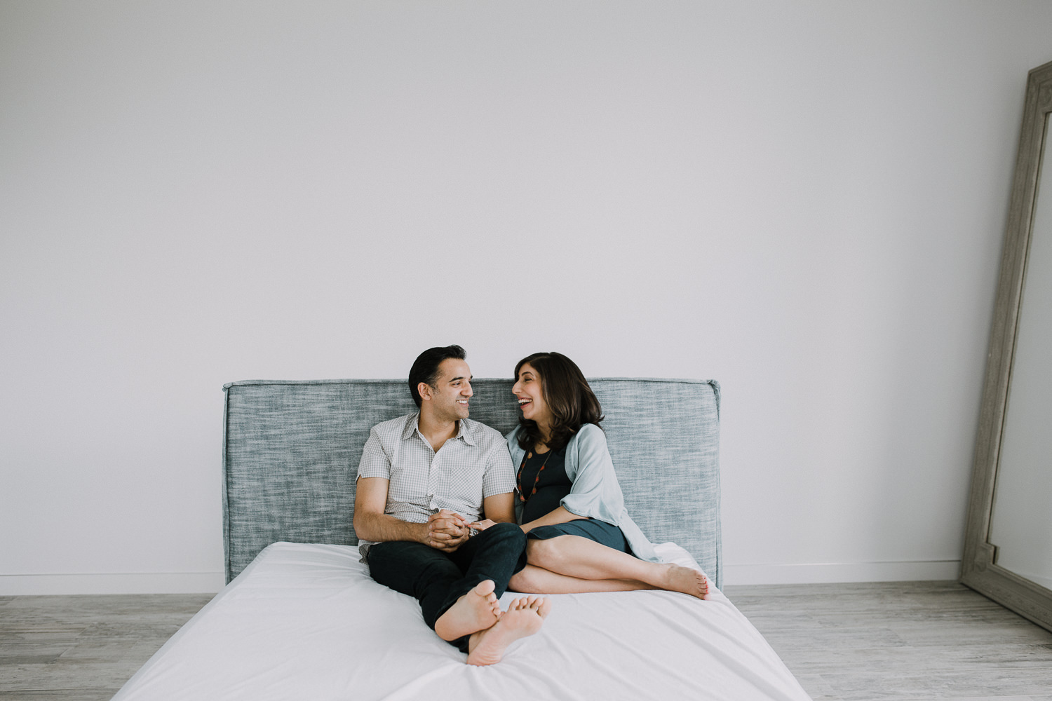 expectant couple sitting on bed laughing and smiling - Newmarket In-Home Photography