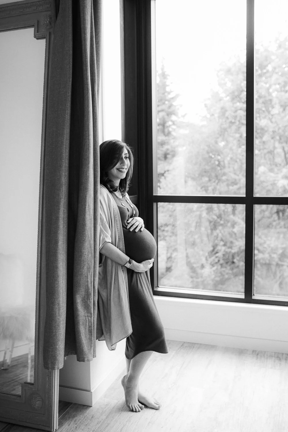 pregnant mother-to-be leans against wall, holding baby bump and smiling - Newmarket Lifestyle Photos