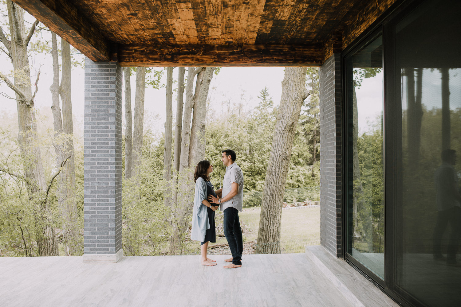 couple standing on patio facing one another, husband bolding wife's pregnant belly - Newmarket Lifestyle Photography