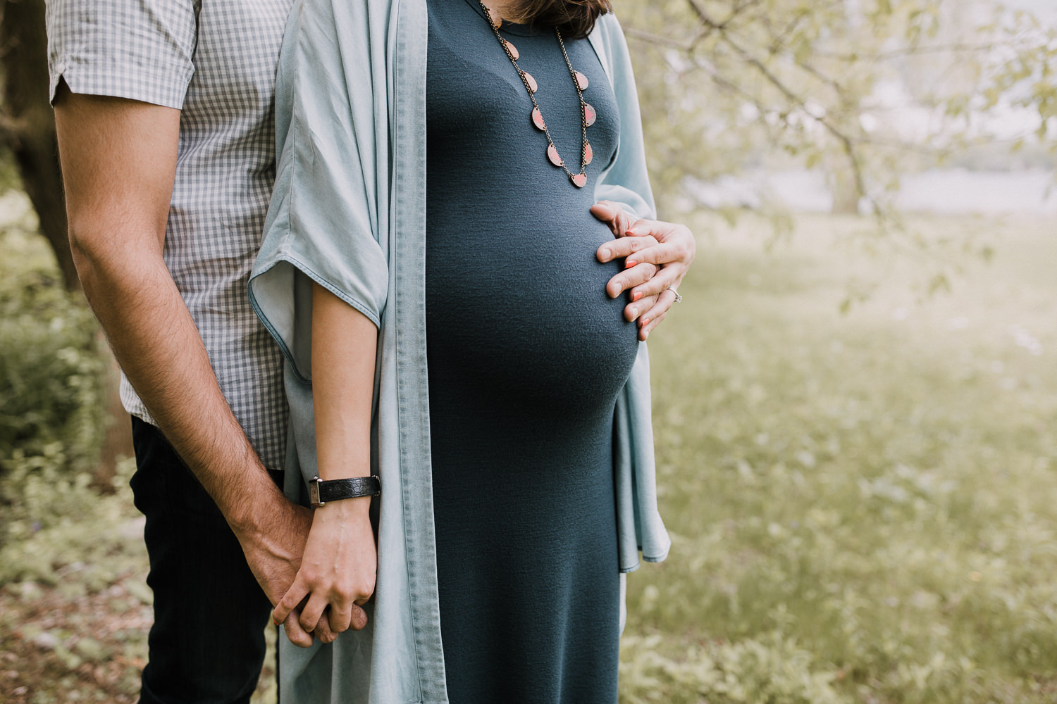 husband standing behind pregnant wife, holding her hand and touching her pregnant belly - Newmarket In-Home Photography