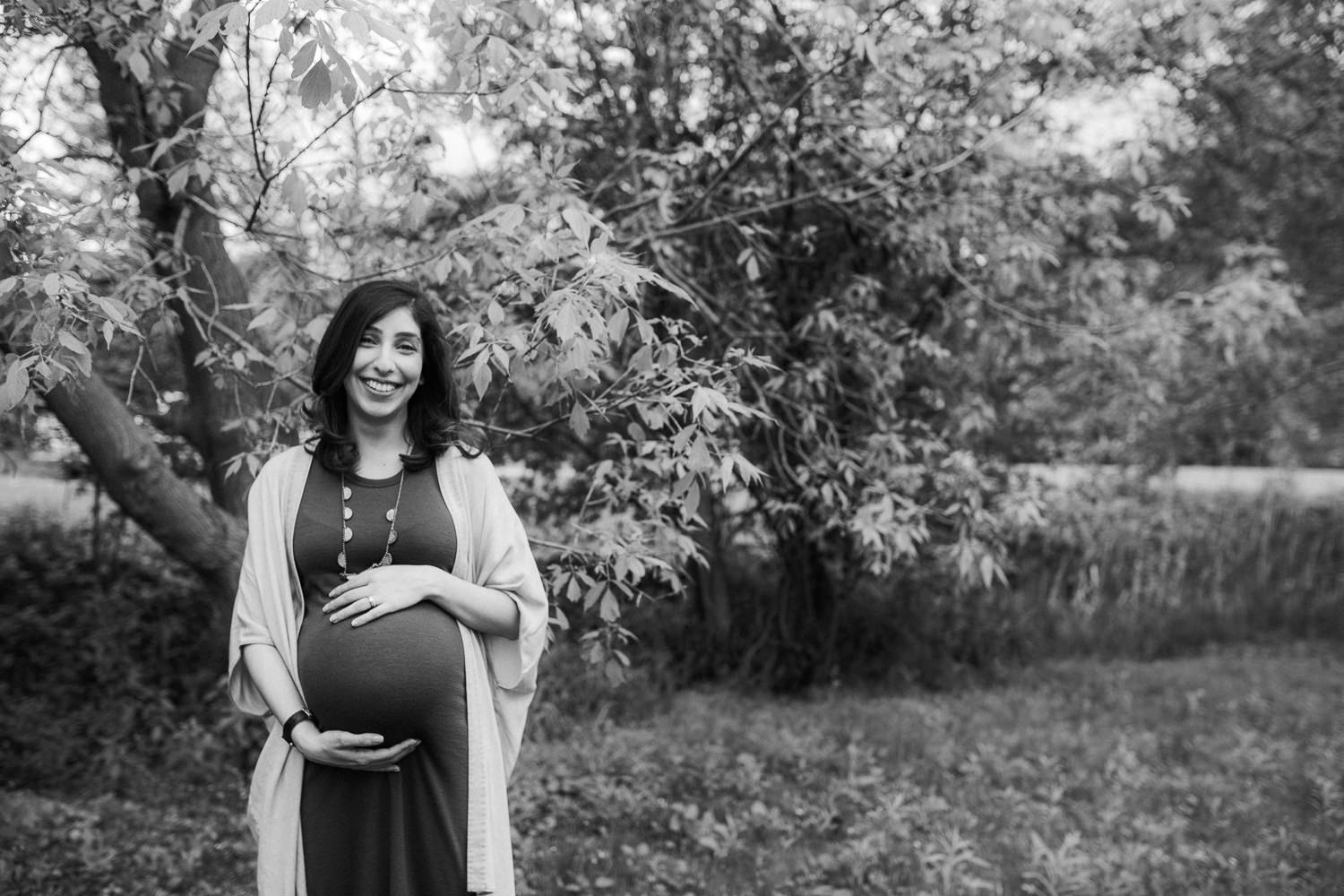 pregnant woman holding her baby belly and smiling at camera - Barrie In-Home Photography