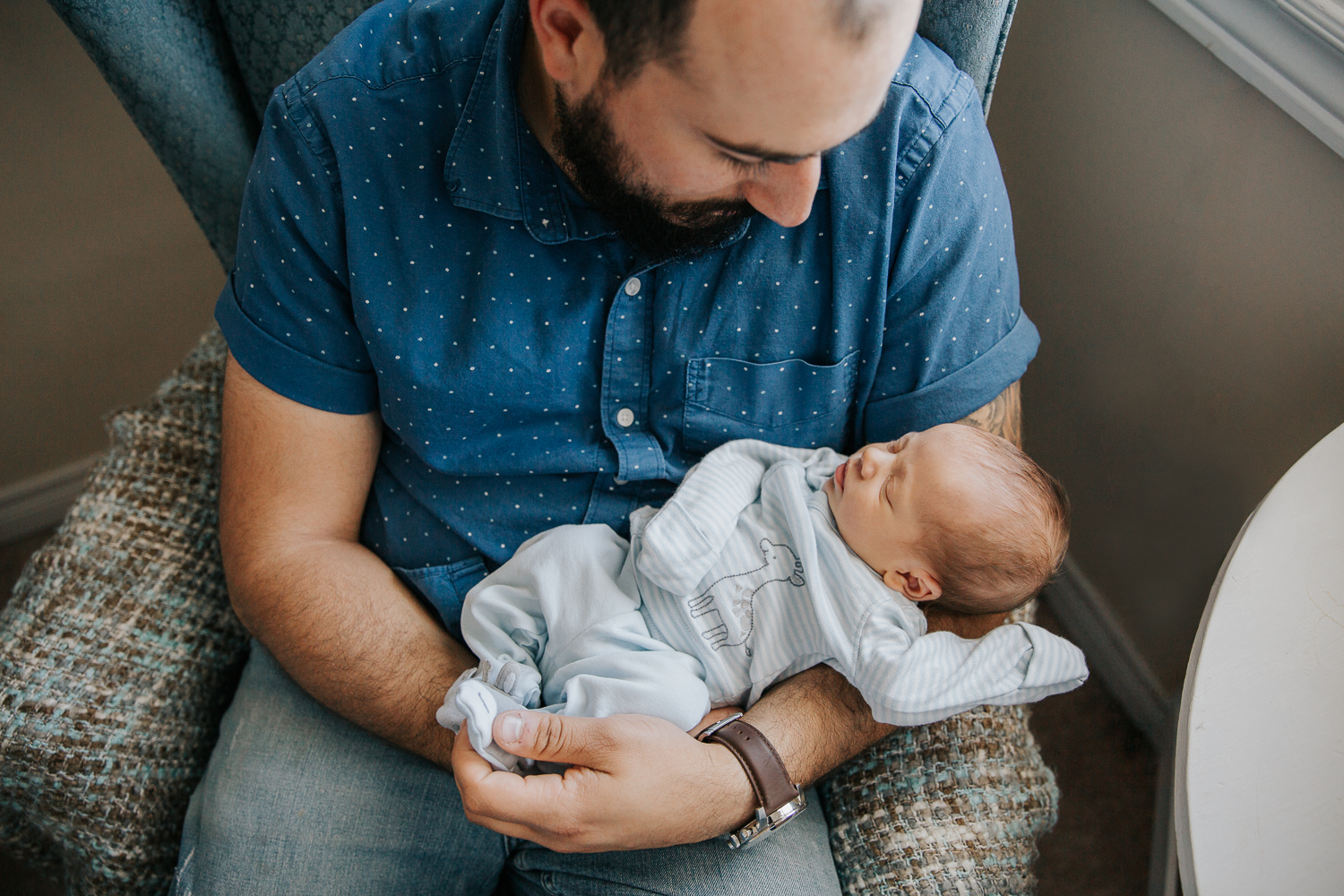 new mom sitting in nursery chair holding 2 week old baby boy in blue sleeper - Stouffville In-Home Photography