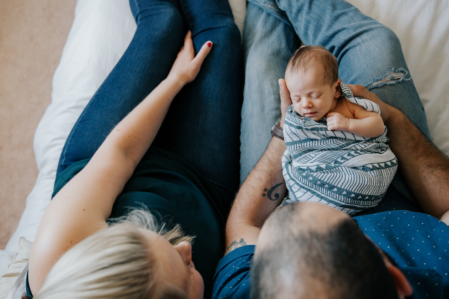 shot from above, parents sitting on bed, 2 week old baby boy in swaddle sleeping in dad's arms - Stouffville Lifestyle Photos