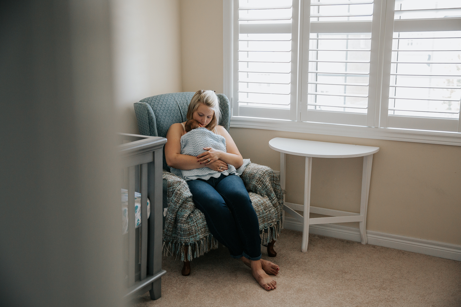 new mom sitting in rocking chair with 2 week old baby boy sleeping snuggled to her chest - Stouffville In-Home Photography