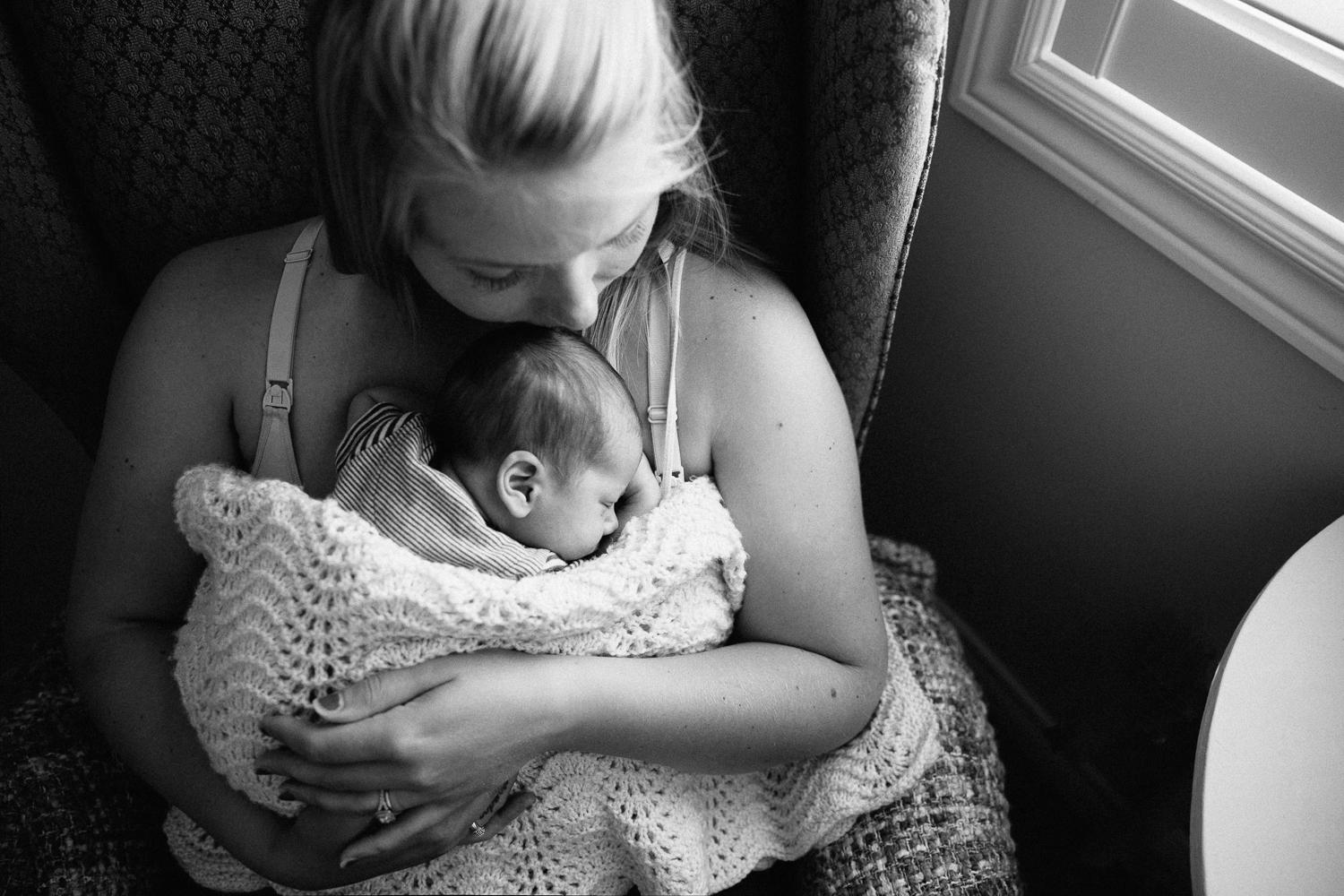 new mom sitting in rocking chair with 2 week old baby boy sleeping snuggled to her chest - Markham Lifestyle Photography