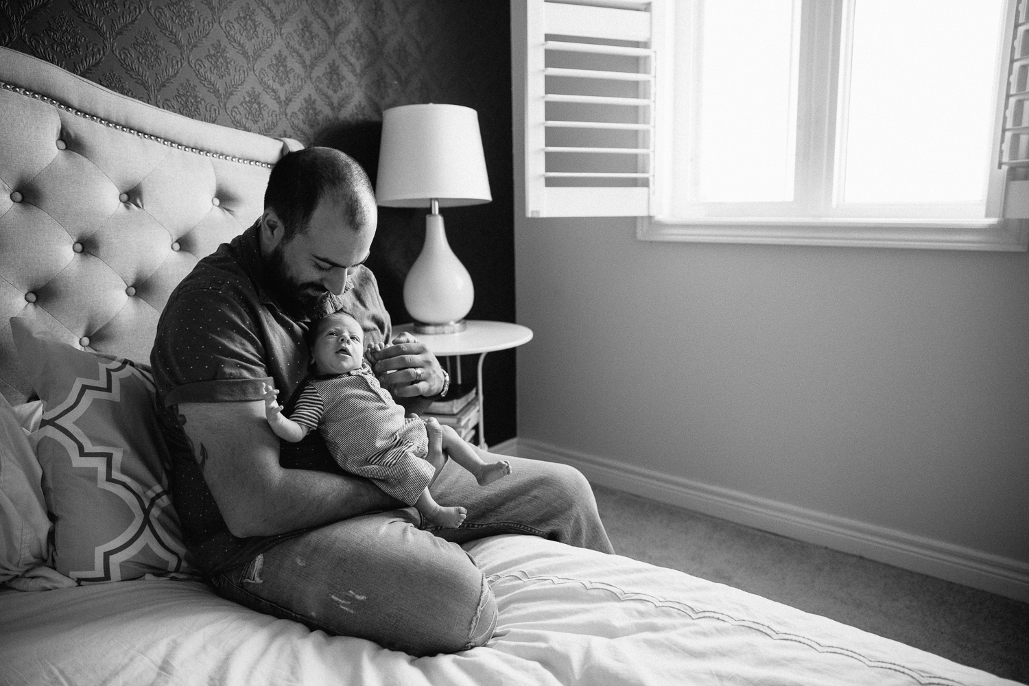 first time dad sitting on edge of bed holding 2 week old baby son - Newmarket Lifestyle Photos