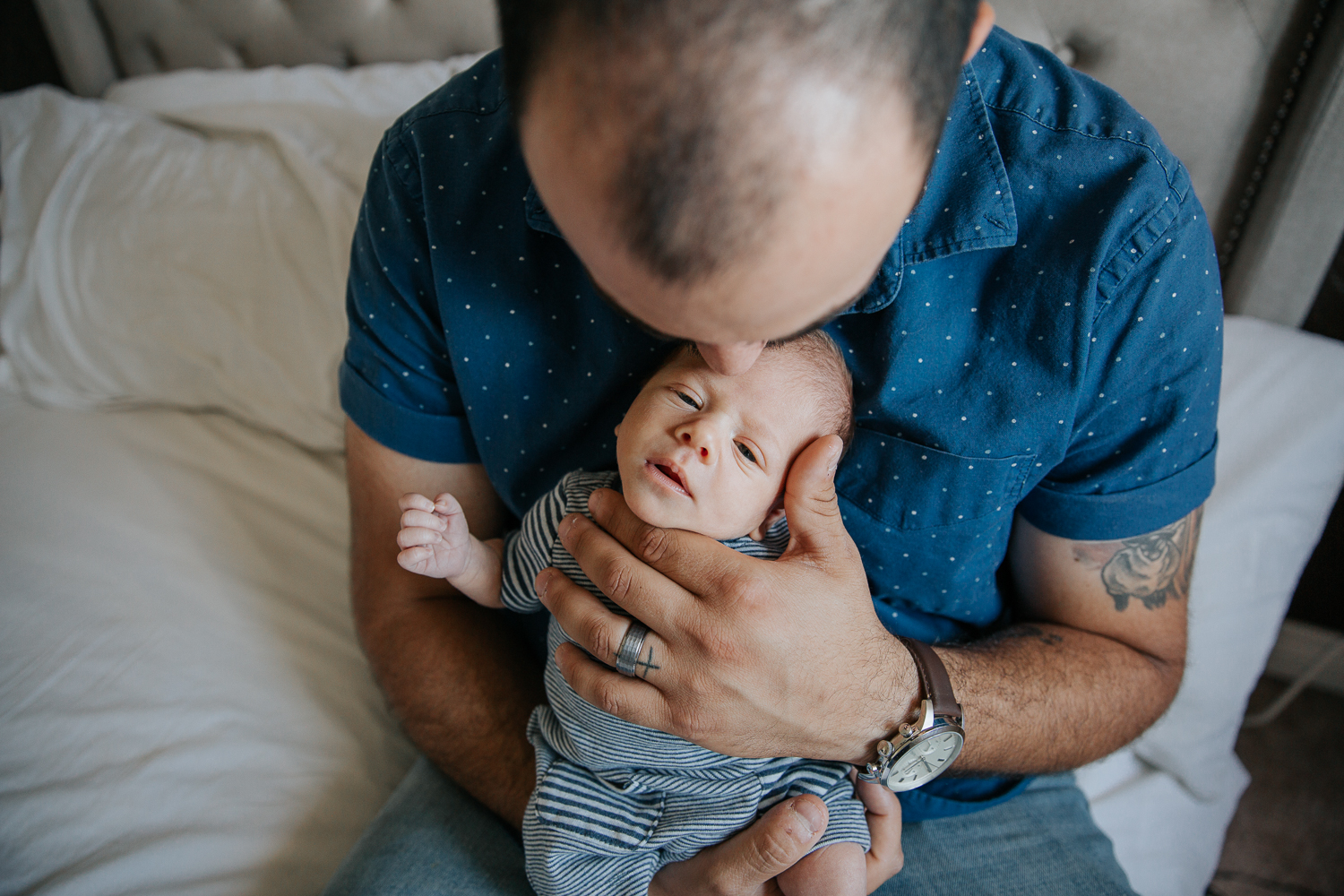 first time dad sitting on edge of bed holding 2 week old baby son, kissing his head - Stouffville Lifestyle Photos