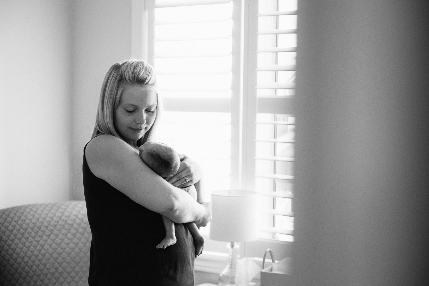first time mom standing in nursery holding sleeping 2 week old baby son - Newmarket Lifestyle Photography