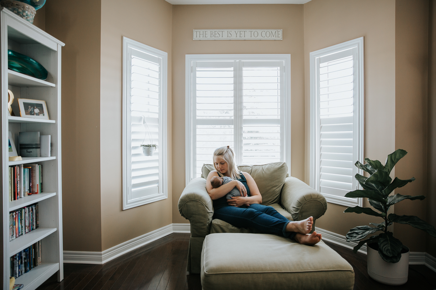 new mom with blonde hair sitting in large chair holding 2 week old baby boy - Markham Lifestyle Photography