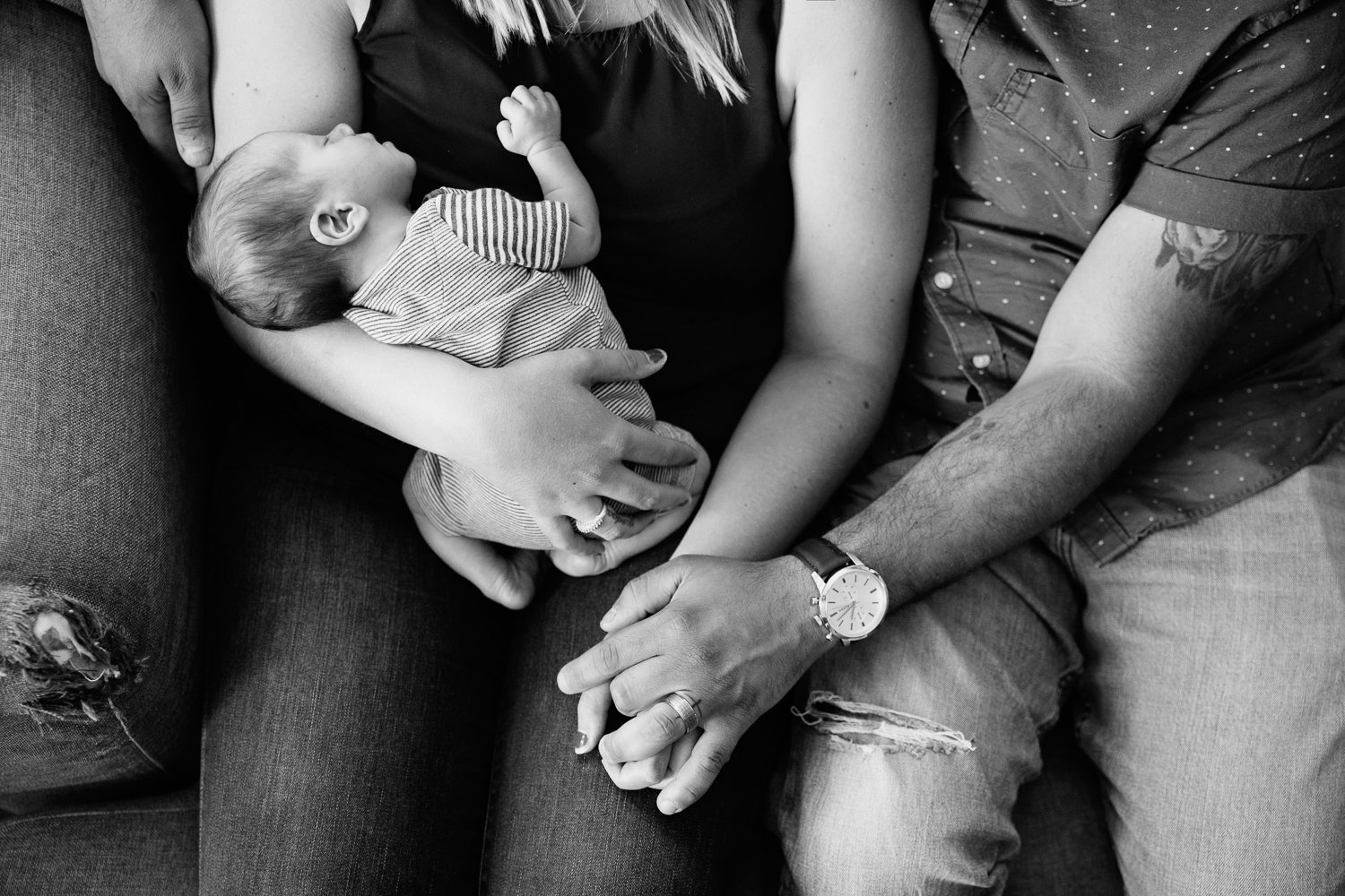 new parents sitting on couch, holding hands, mom holding 2 week old baby boy - Stouffville In-Home Photography
