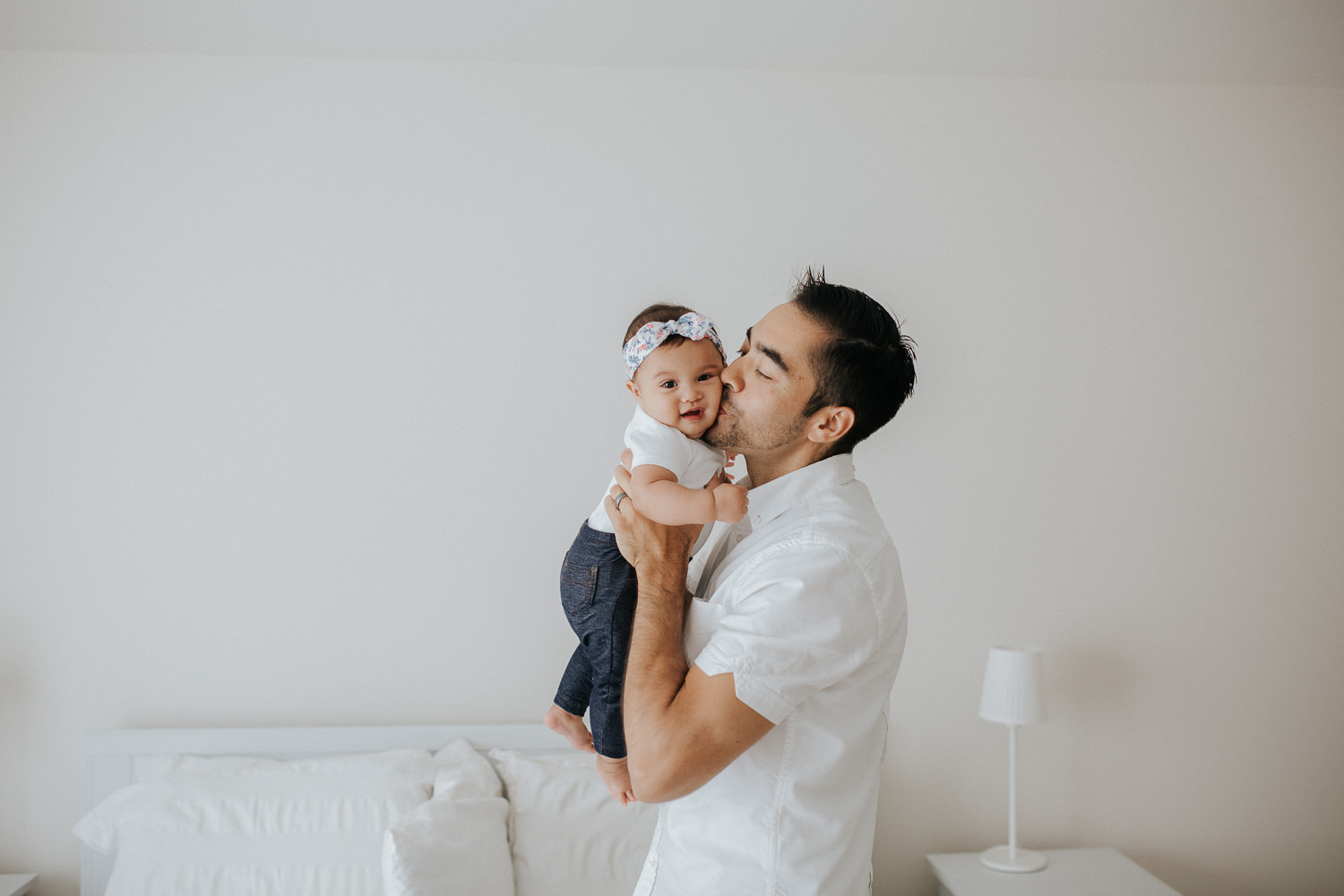 dad lifting up 6 month old baby daughter and kissing her on cheek, baby looking at camera - Markham Lifestyle Photography