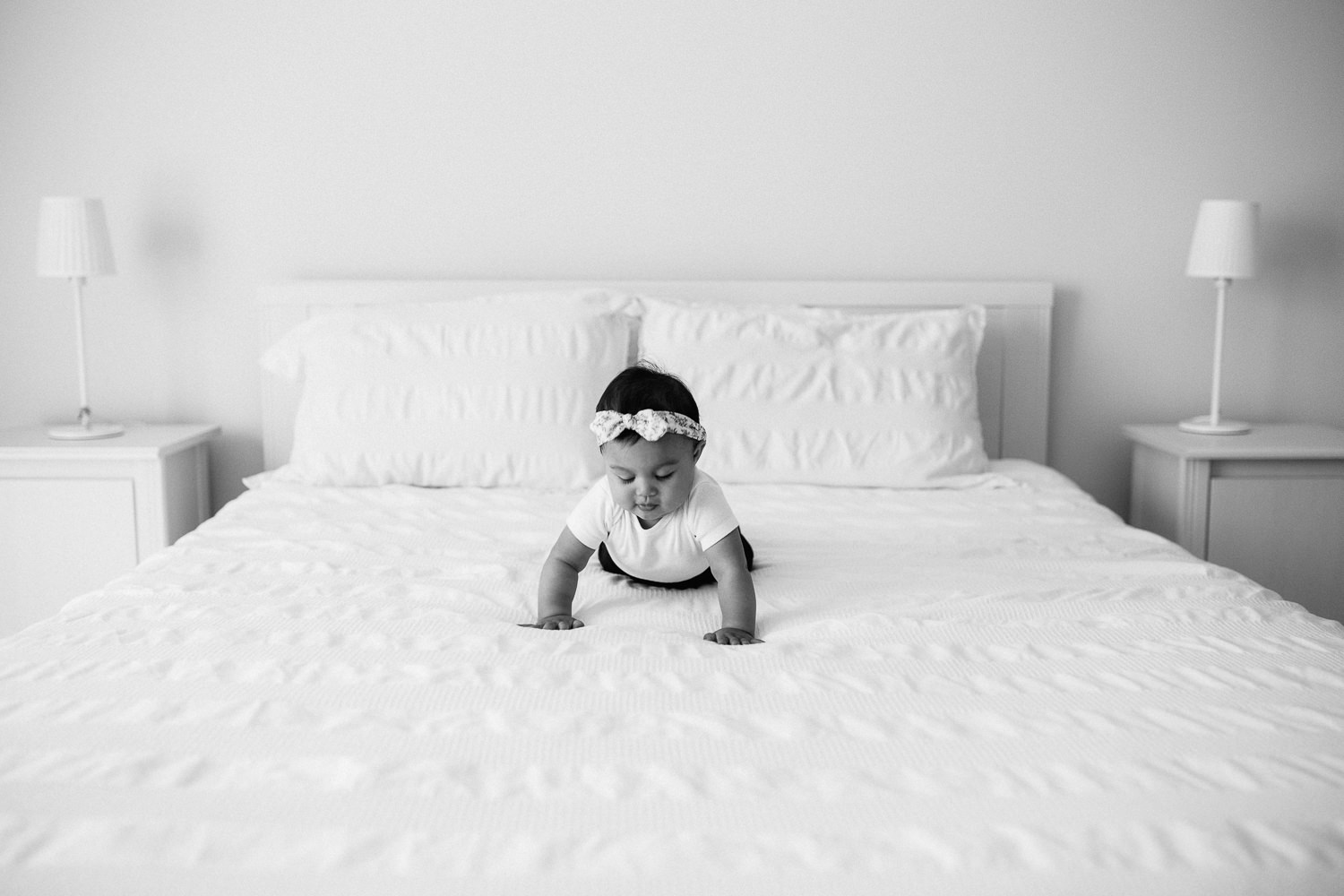 6 month old baby girl with floral headband on crawling on white bed - Stouffville Lifestyle Photography