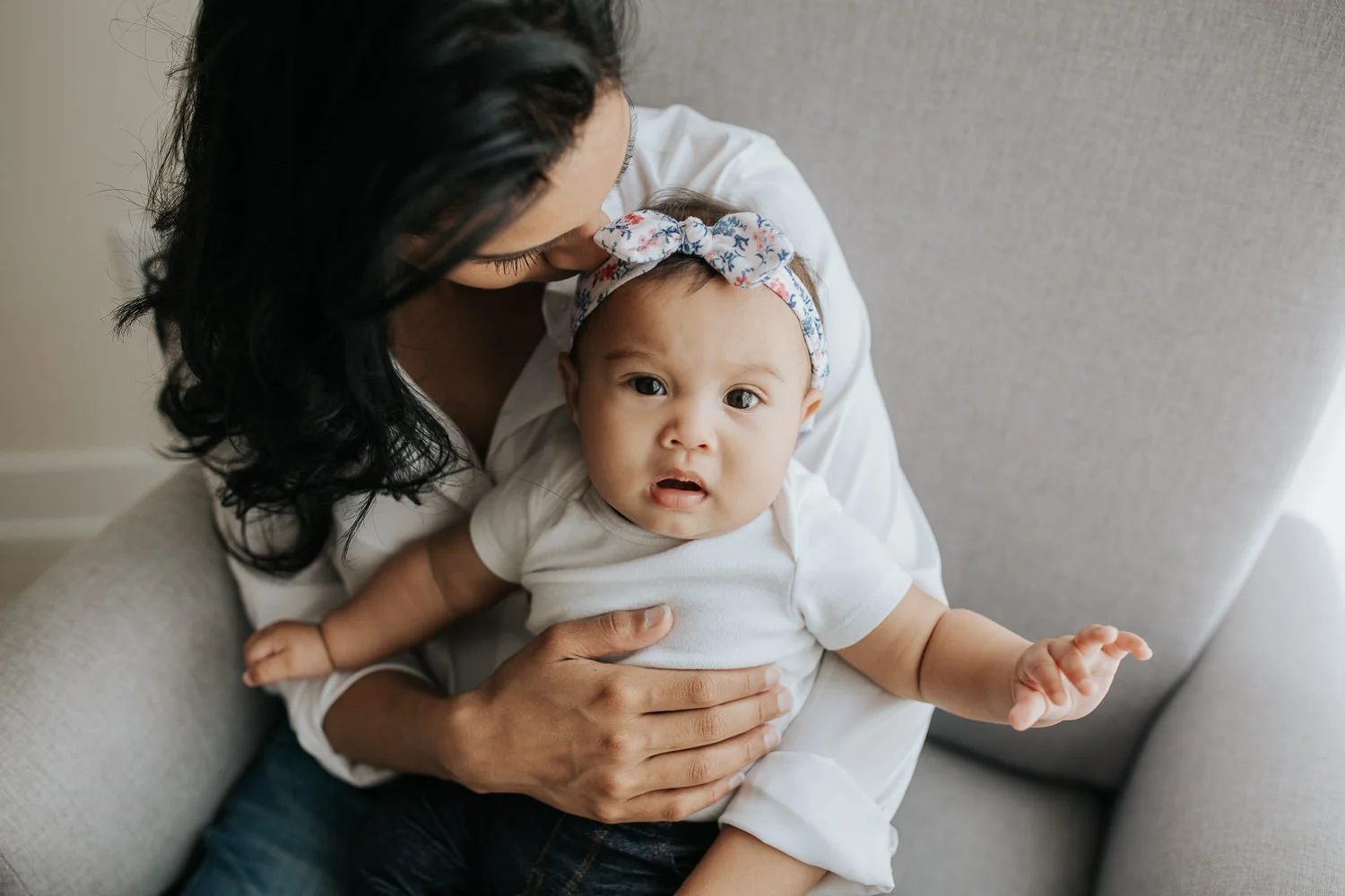 Newmarket In-Home Photographymom sitting in glider holding 6 month old daughter in her lap, baby girl looking at camera -