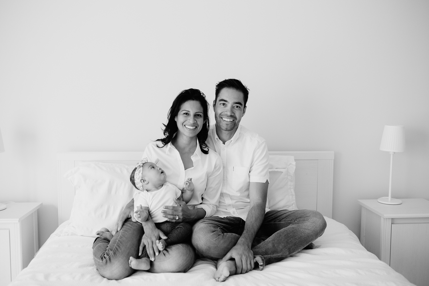 family of 3 with 6 month old baby girl sitting on bed smiling at camera, baby looking up at mom - Newmarket In-Home Photos