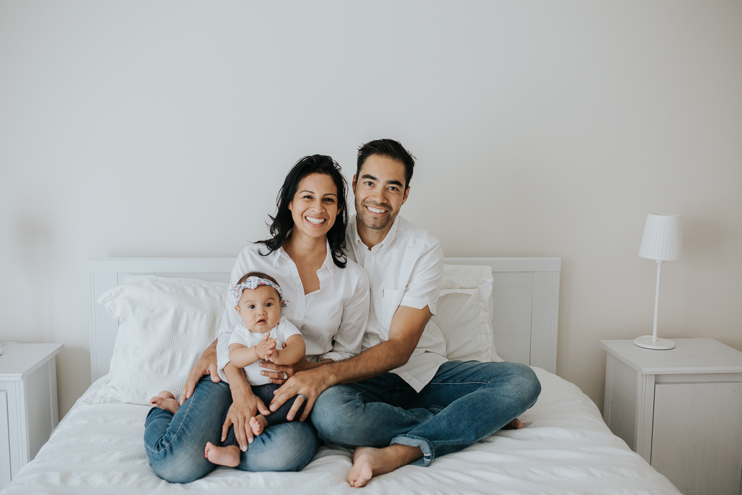 family of 3 with 6 month old baby girl sitting on bed smiling at camera - Stouffville In-Home Photos