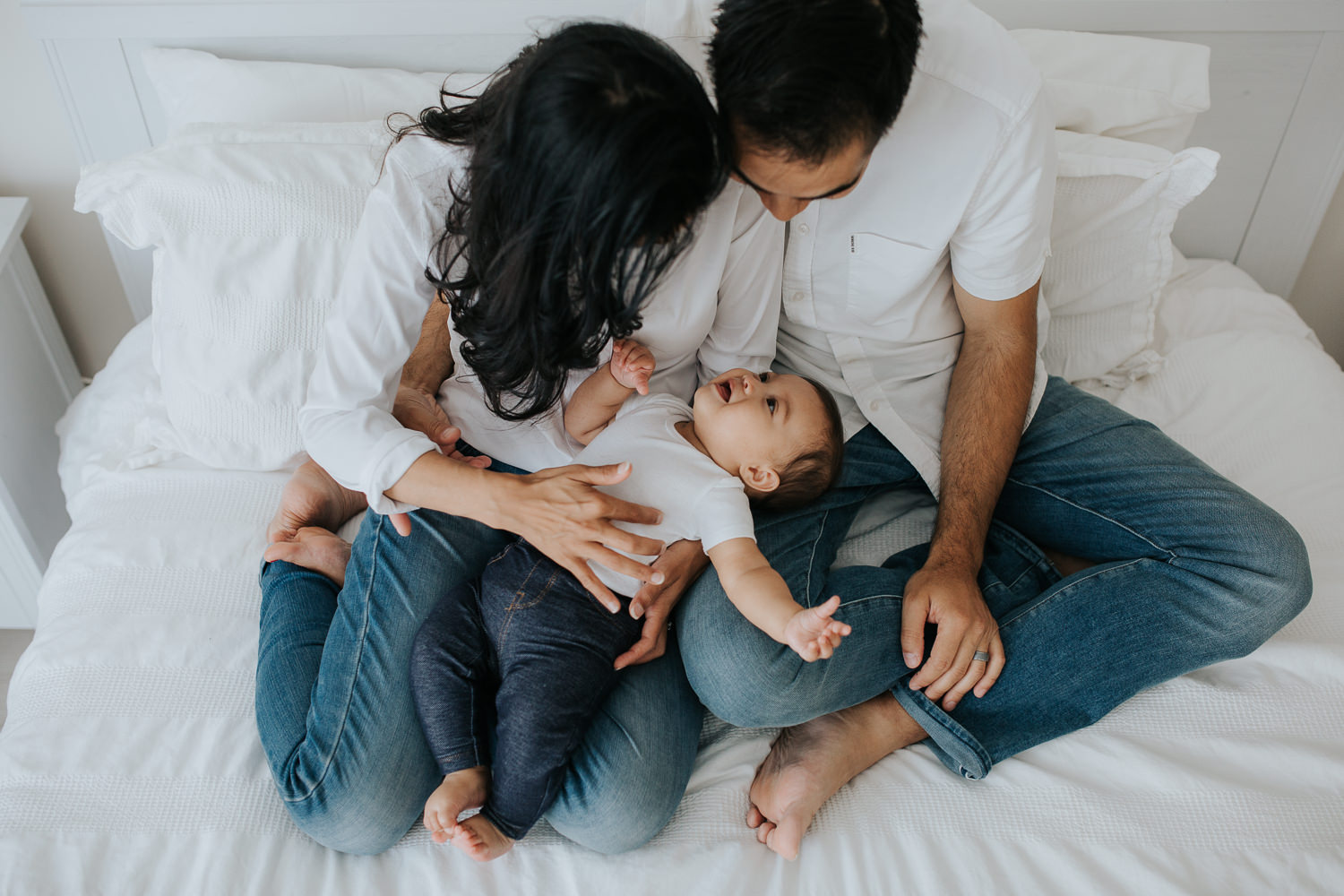 parents sitting on bed, baby girl lying in mom and dad's laps - Barrie In-Home Photos