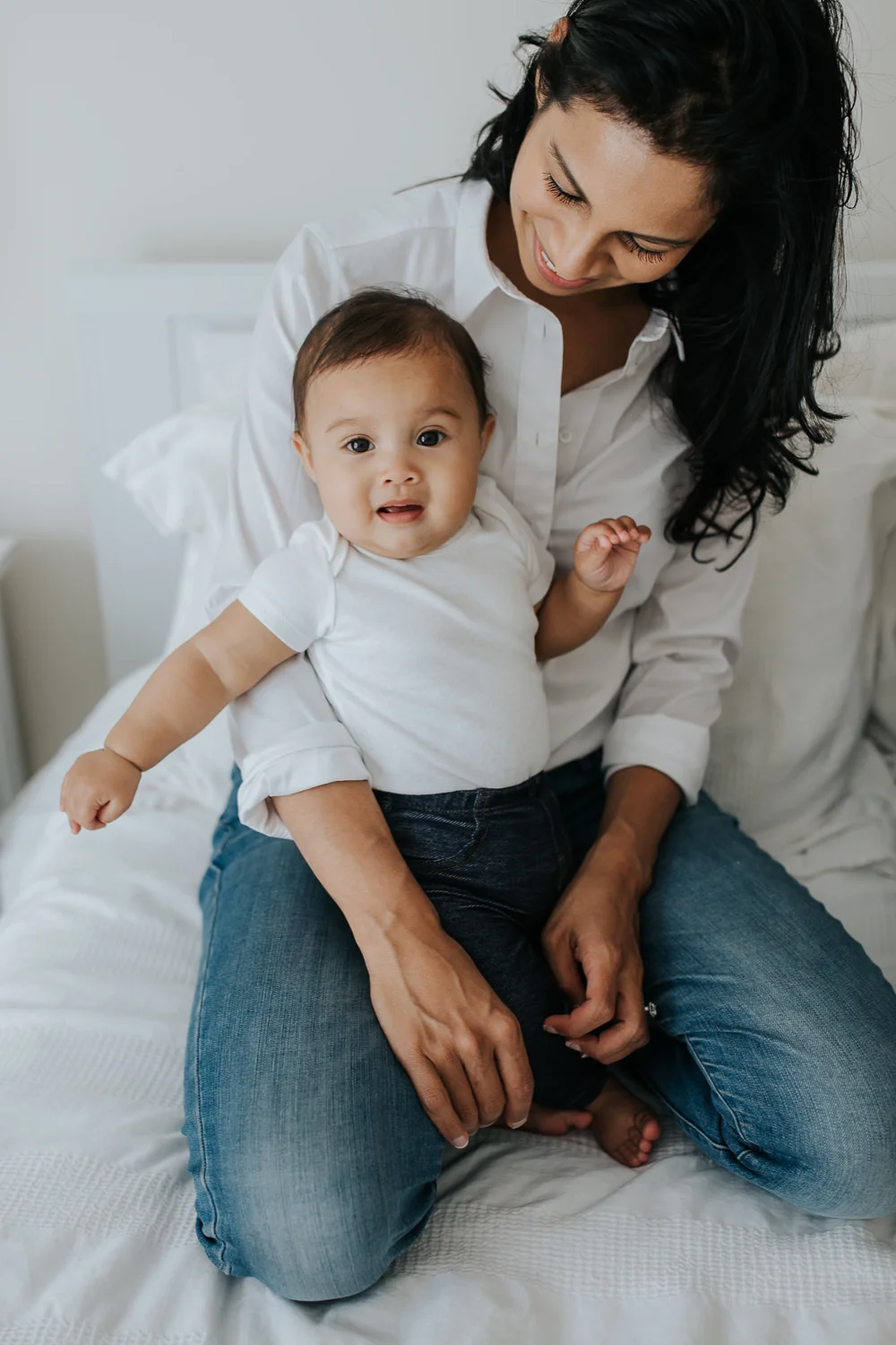 6 month old baby girl sits in mom's lap on bed, looking at camera - Barrie Lifestyle Photos