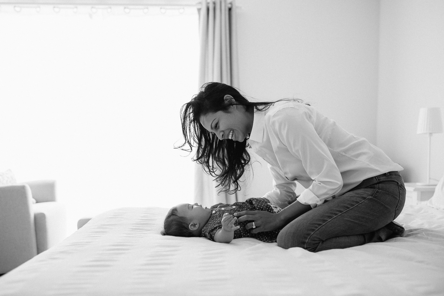 6 month old baby girl lying on bed, mom leaning over her smiling - Markham Lifestyle Photography