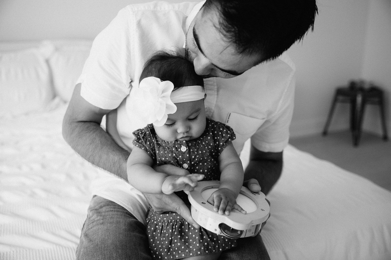 father sitting with 6 month old baby girl in his lap, kissing the top of her head - Markham In-Home Photography