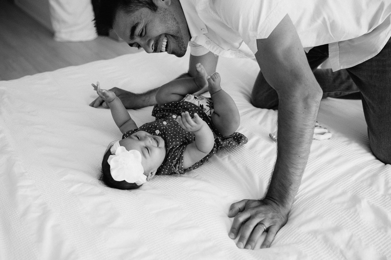 6 month old baby girl lying on bed laughing as dad leans over, tickling her - Barrie In-Home Photos