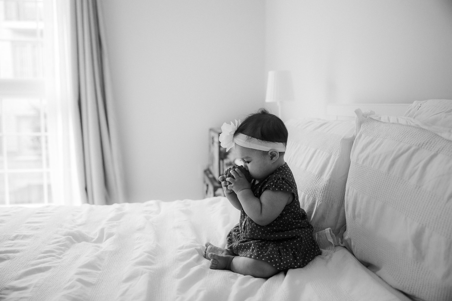 6 month old baby girl sitting on bed chewing on toy - Stouffville Lifestyle Photos